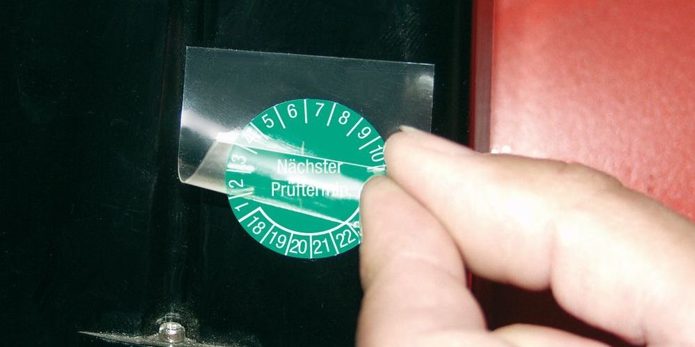 Übertrag der Plakette mit einer Folie. Nach Verklebung zerreißt Plakette in kleine Stücke